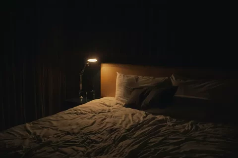 Made bed with a lit bedside lamp and simple nightstand, suggesting a calm sleep environment.