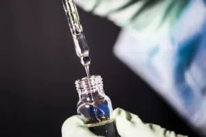 Gloved technician using pipette and glass vial during clinical trial preparation